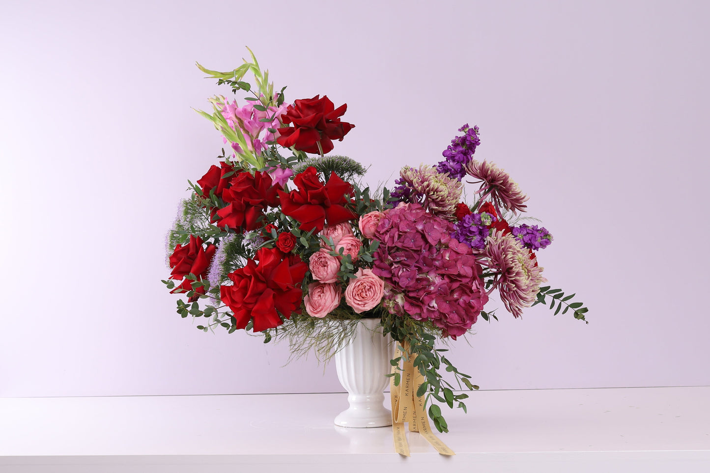 Rouge Velours - red roses, mauve hydrangeas and purple flowers in white urn vase